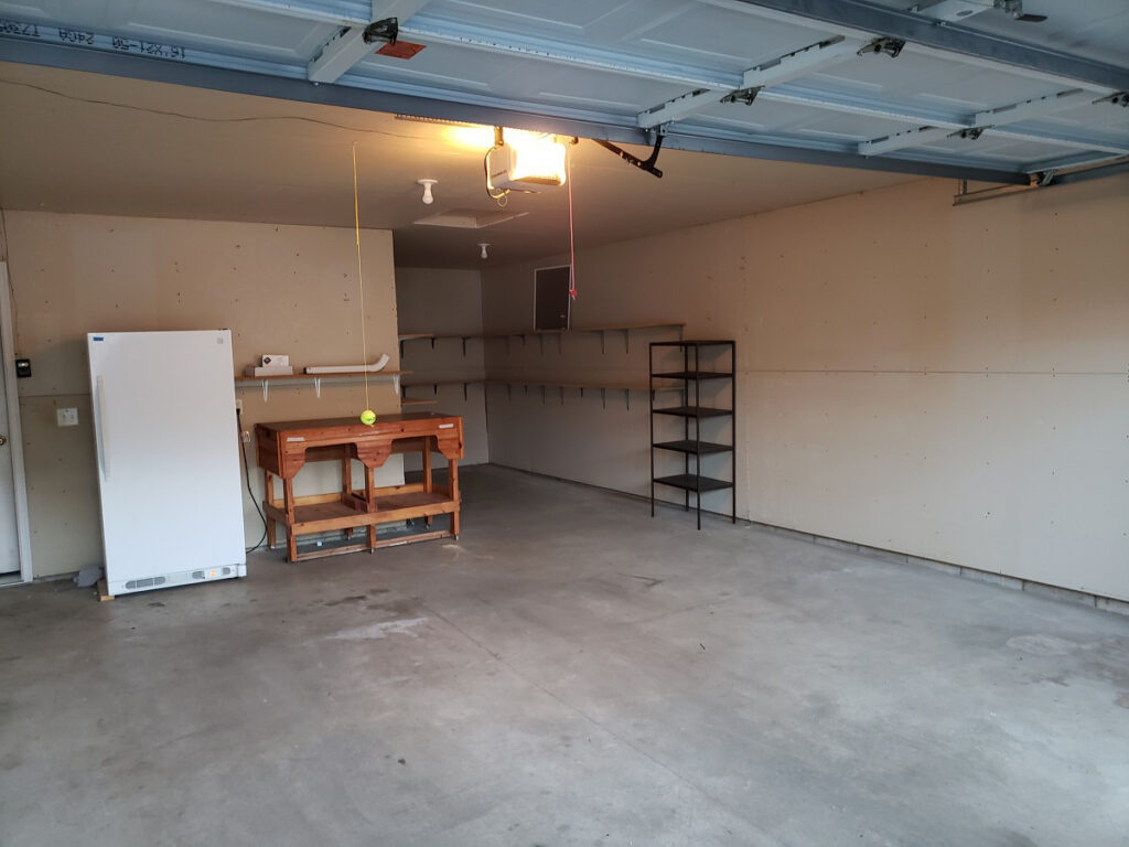 A completely cleared and swept garage showing a clean floor and organized shelving after a professional junk removal service.