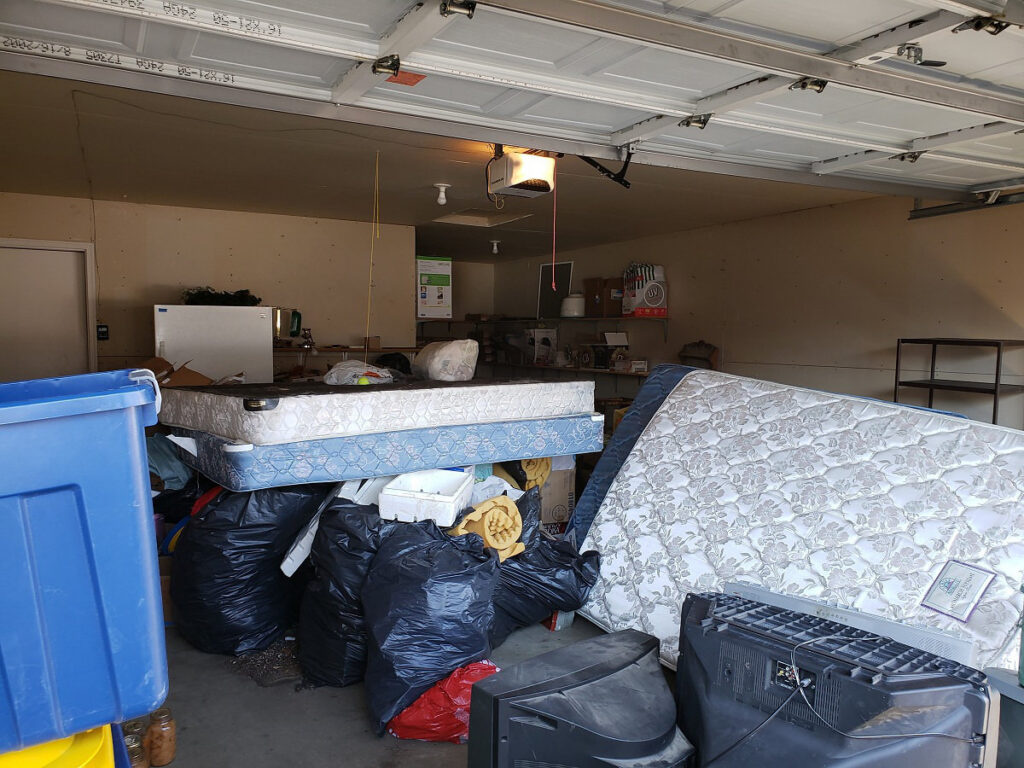 A garage filled with unwanted junk, including old mattresses, large CRT televisions, and trash bags before a professional cleanout.