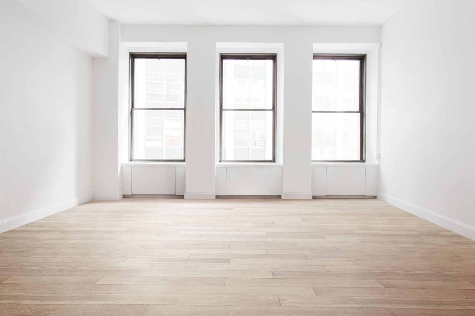 A bright, completely empty apartment room with pristine hardwood floors and large windows, ready for a new tenant after a fast cleanout.