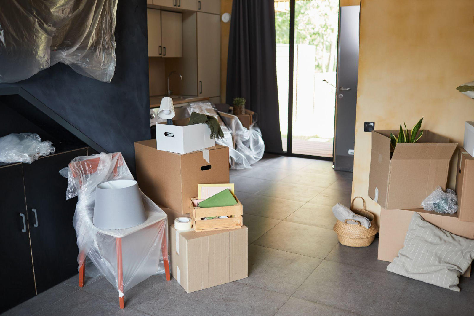 A messy rental unit filled with leftover moving boxes, plastic-wrapped furniture, and a mattress, causing a delay in the tenant turnover process.