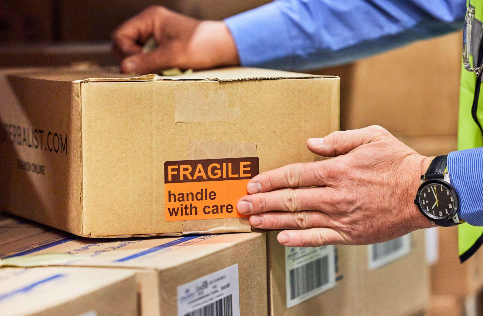 A person holding a cardboard box with an orange label reading Fragile - Handle with care for delicate household items.