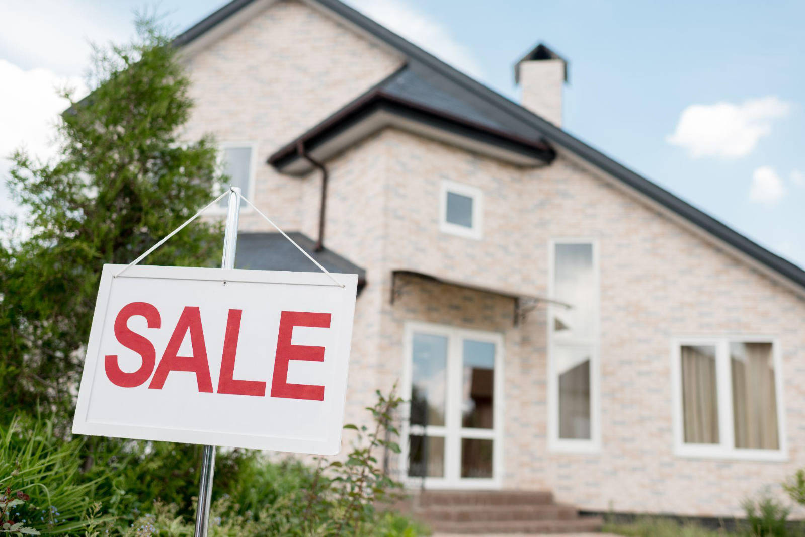 A white sign with red letters reading SALE standing in the front yard of a home ready to be listed after a house cleanout.