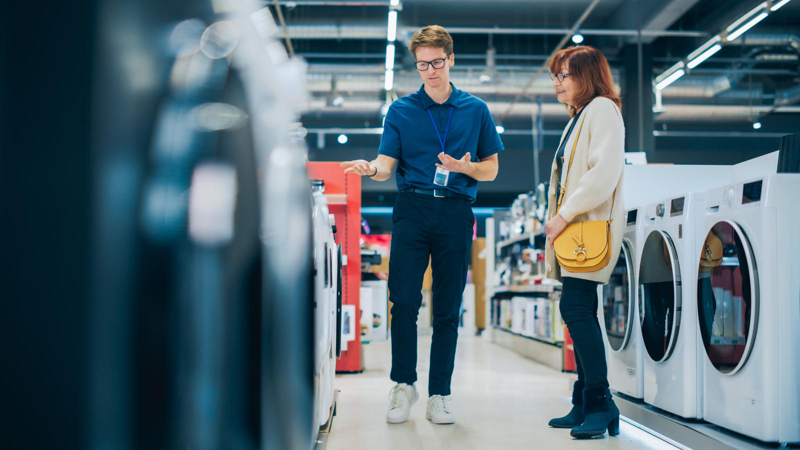 A customer speaking with a retail associate in an appliance store showroom while browsing new washing machines.