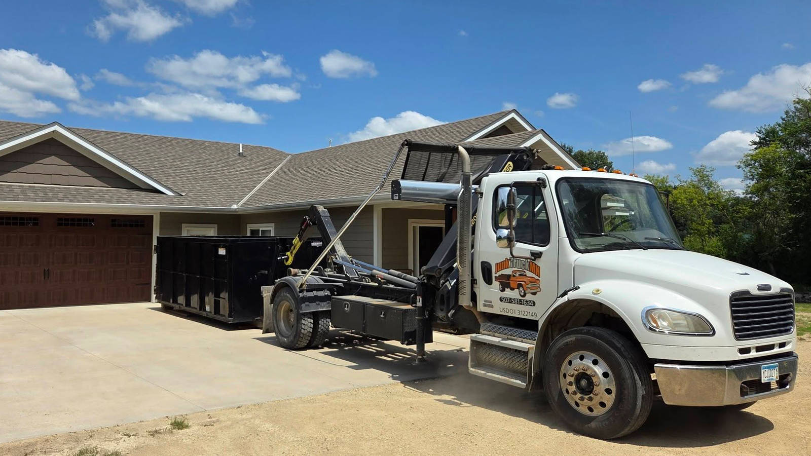 Junk Truck MN hook-lift truck dropping off a residential dumpster in a driveway for construction cleanup.