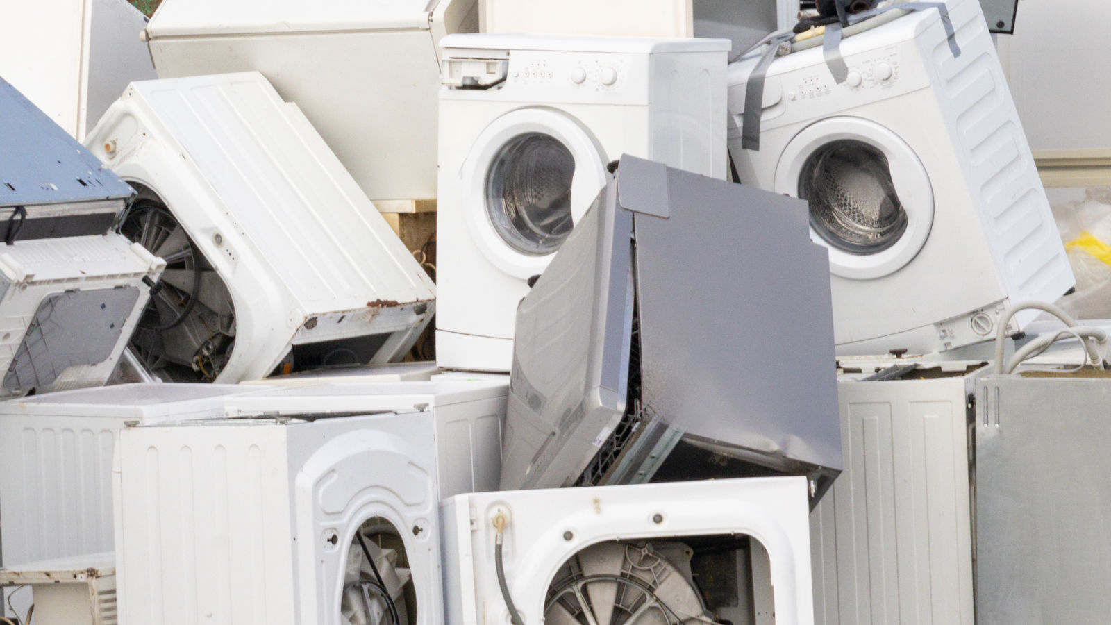 A pile of discarded washing machines and household metal appliances stacked together at a scrap metal recycling facility.